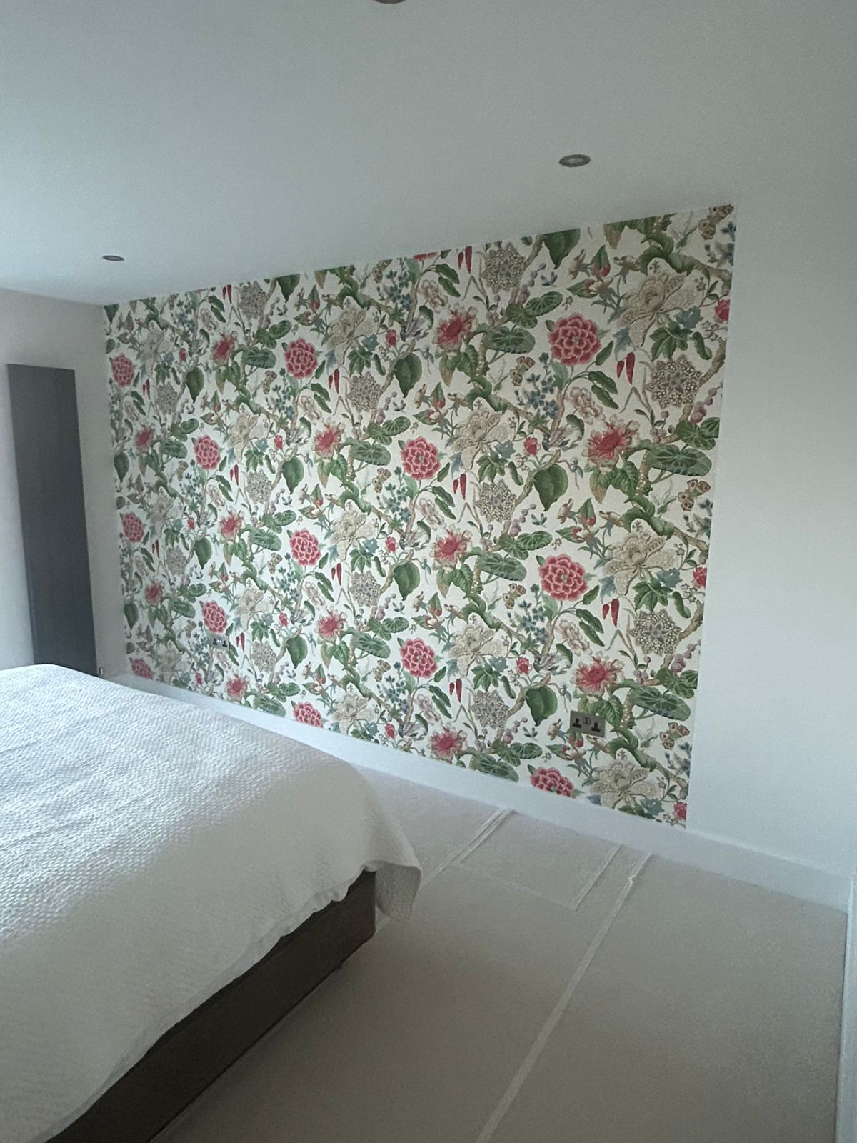 Angled view of a finished floral wallpaper feature wall behind a bed