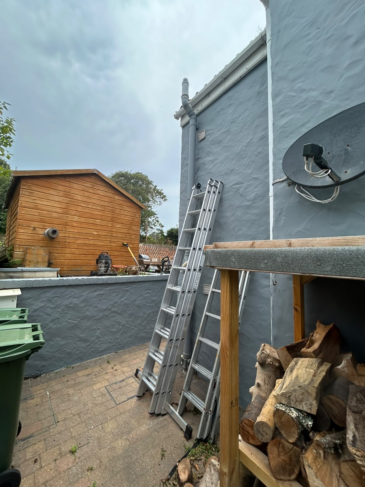 Ladders in place against slate grey render during exterior repaint