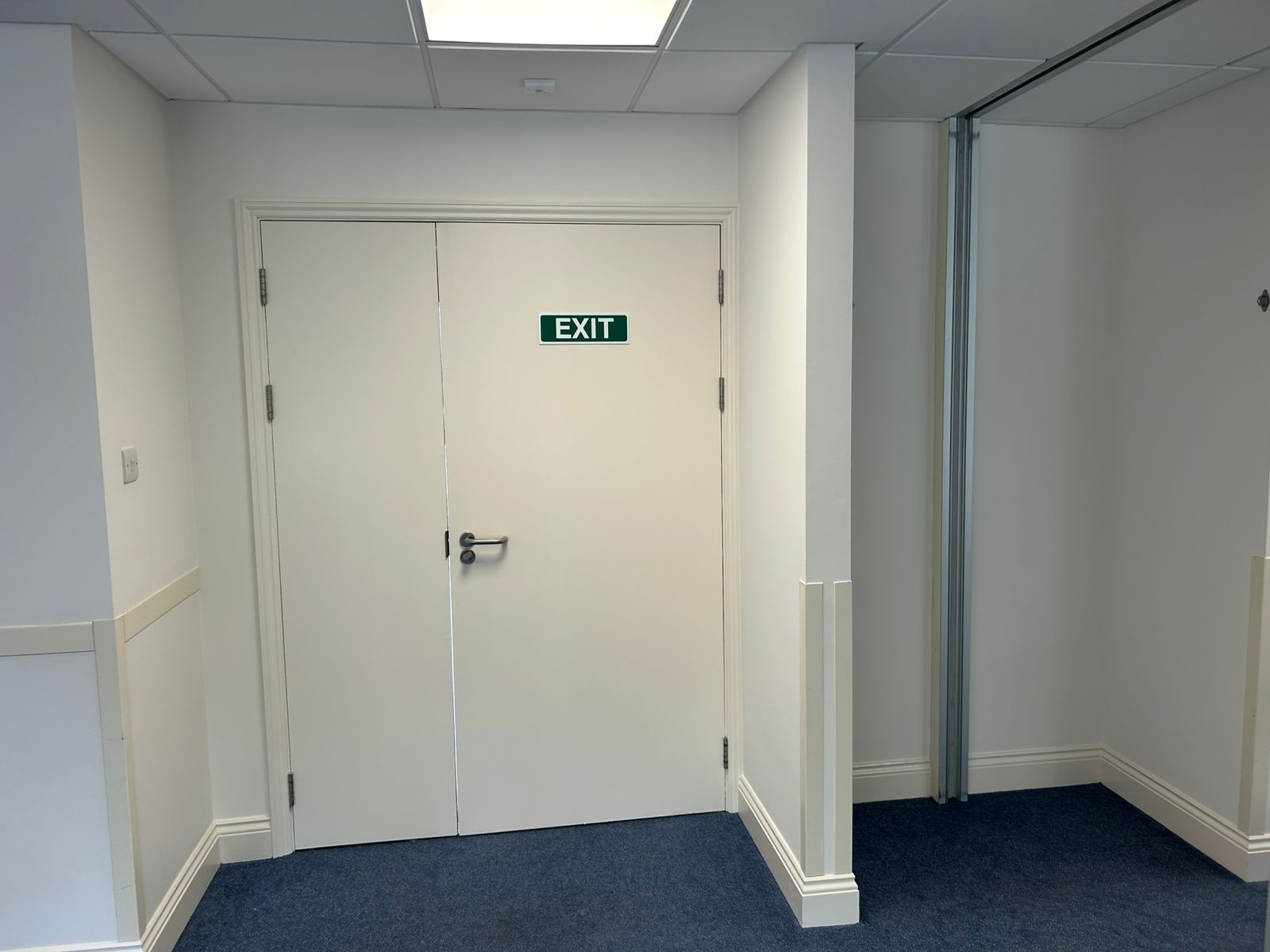 Fire exit doors freshly painted white with clean dado rail and skirting