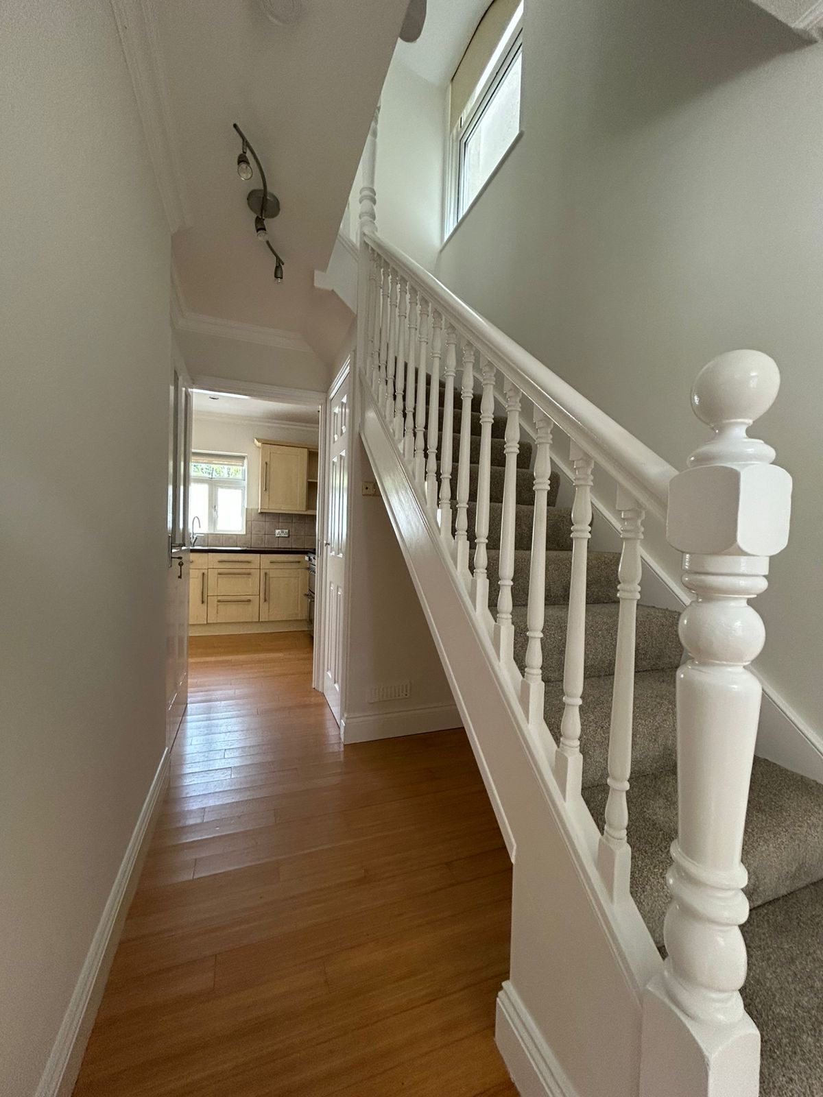 Hallway with white banisters, wood floor and view through to kitchen