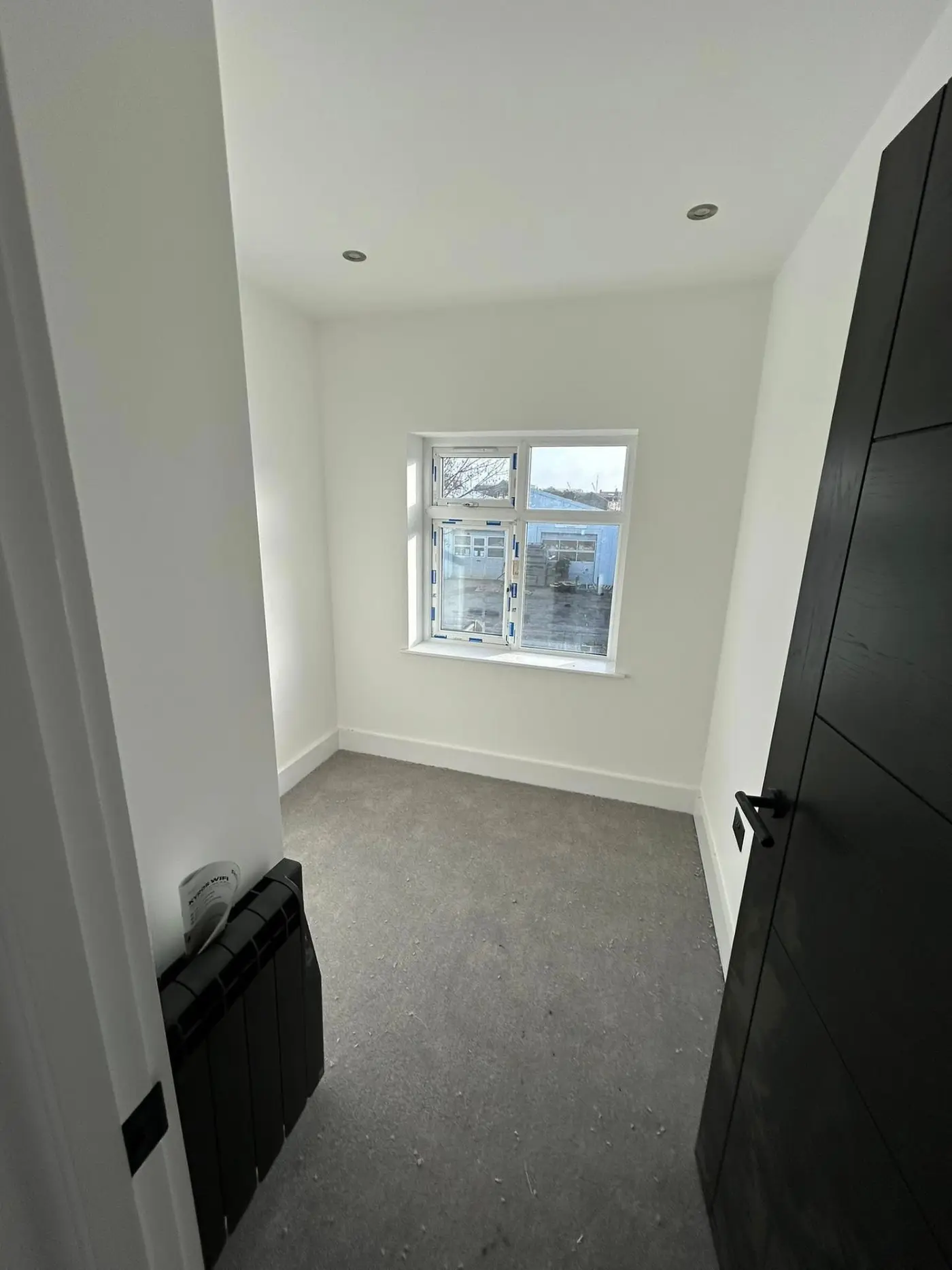 Small bedroom with window, white walls and dark door