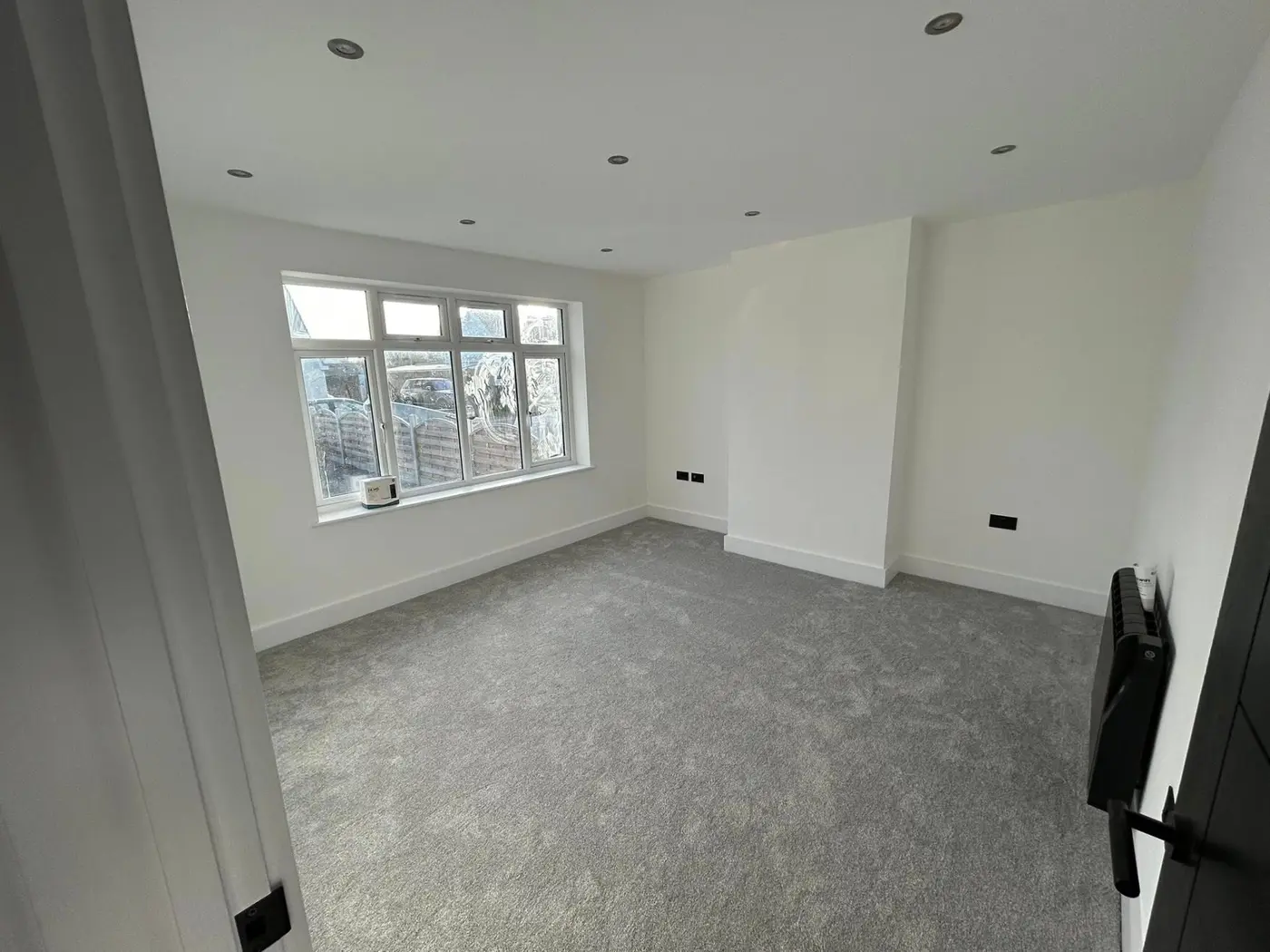 Bedroom with large window, white walls and grey carpet