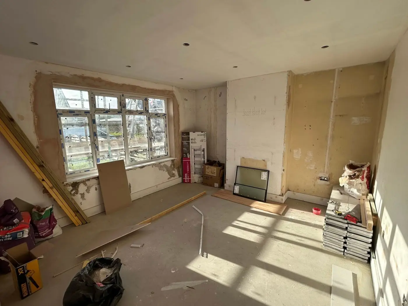 Before — room with stripped walls, plasterboard and building materials