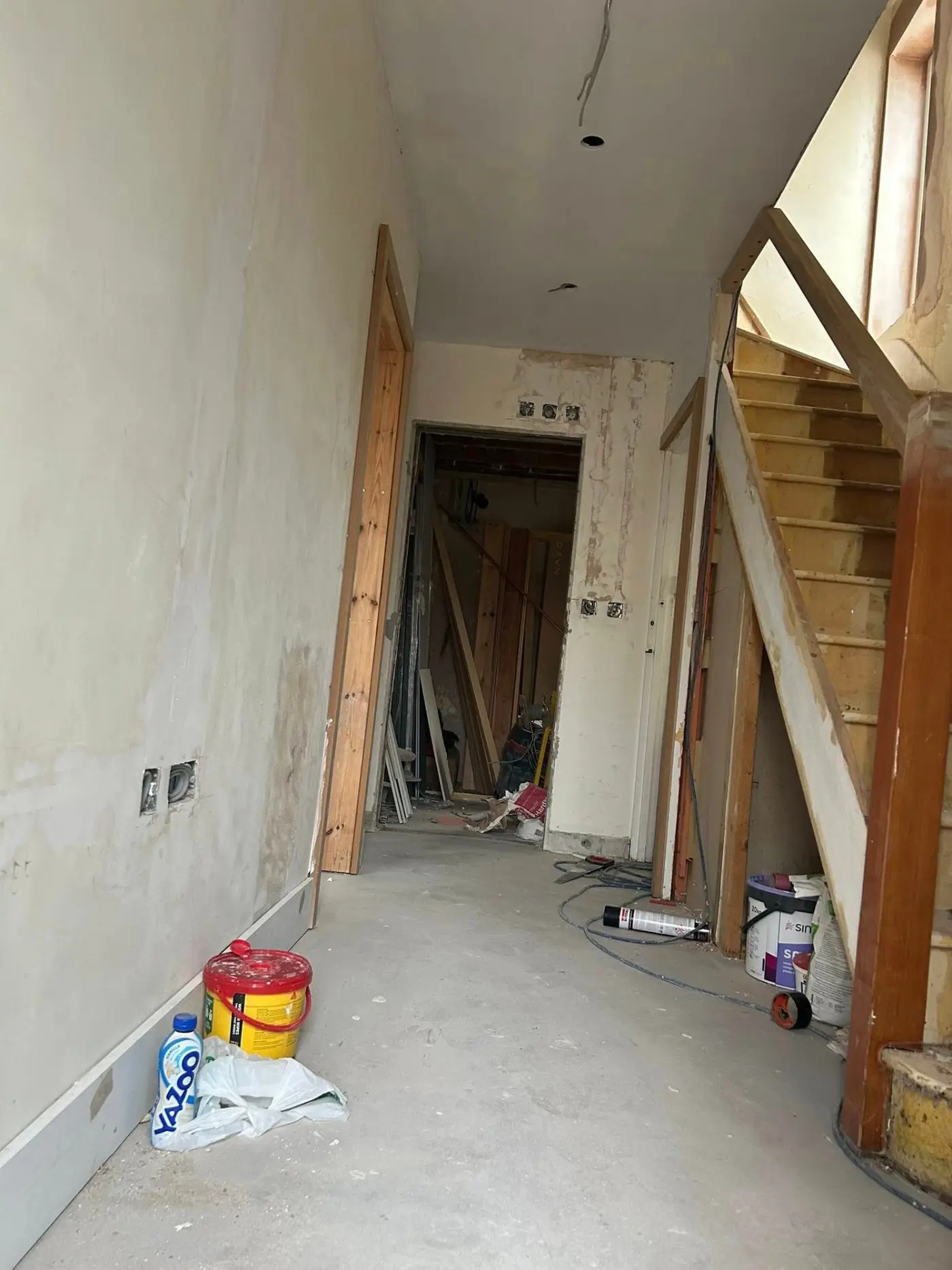 Before — hallway with bare plaster, staircase and paint supplies