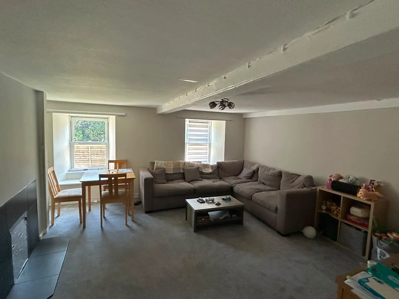 Living room with grey sectional sofa, dining table by window and freshly painted beams