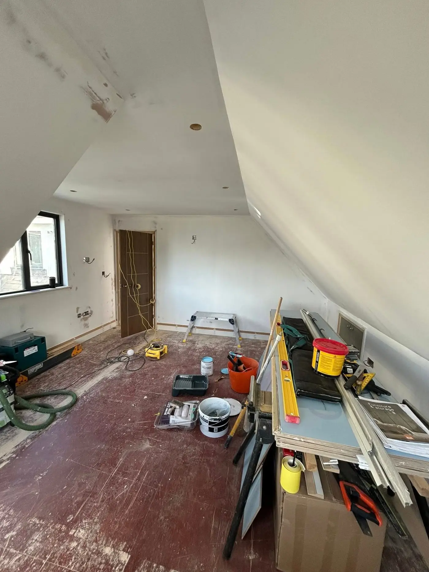 Loft room before — bare plaster walls with tools and materials